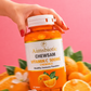 Hand holding a bottle of Aimsbiotic Chewsam Vitamin C 500MG chewable tablets with oranges in the background.